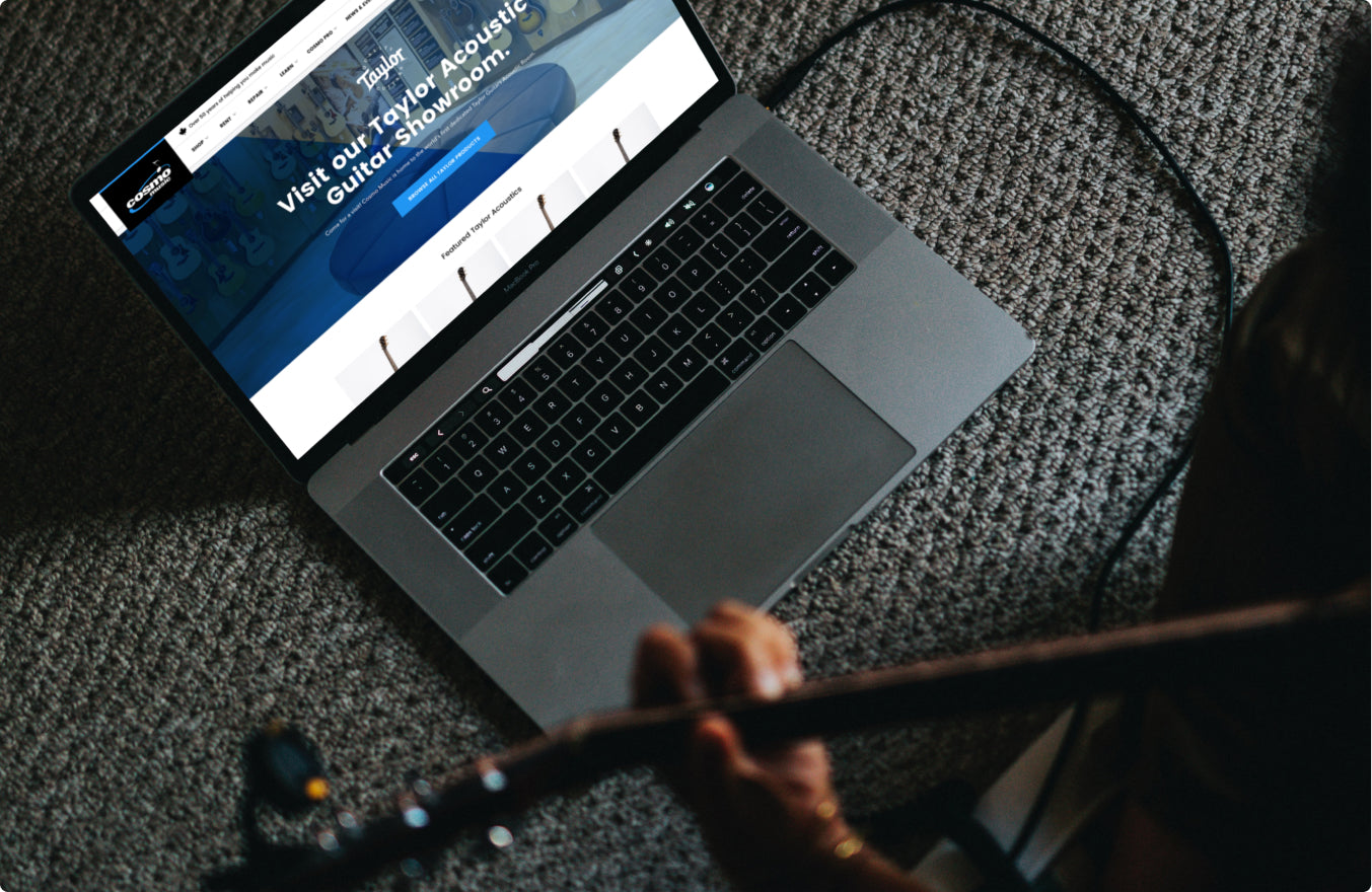 Laptop showing Cosmo Music site, hands playing guitar.