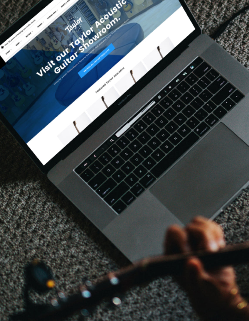 A laptop displaying Cosmo Music's website with someone playing a guitar in the foreground.