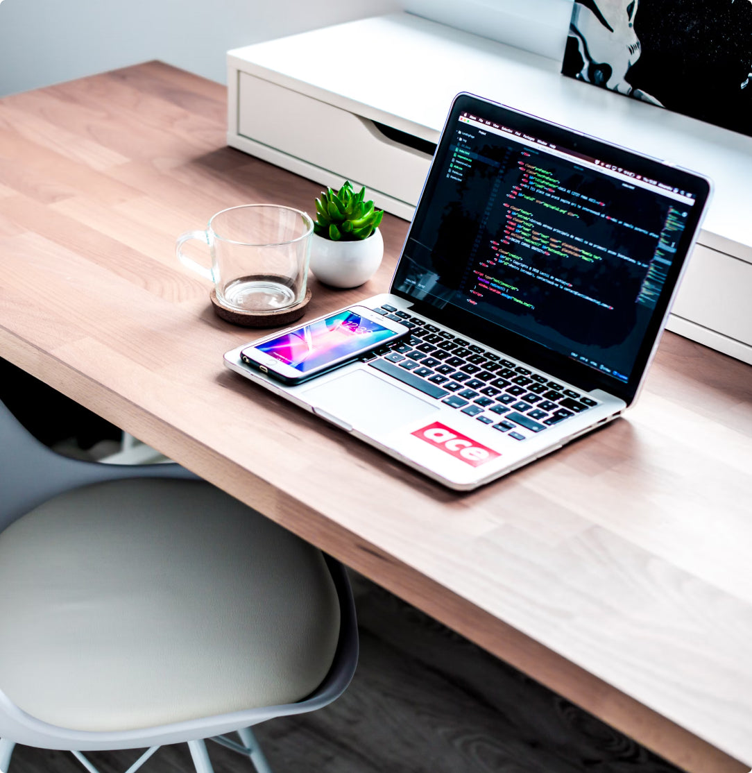 A tidy desk with a laptop showing code, a smartphone, an empty mug, and a plant.