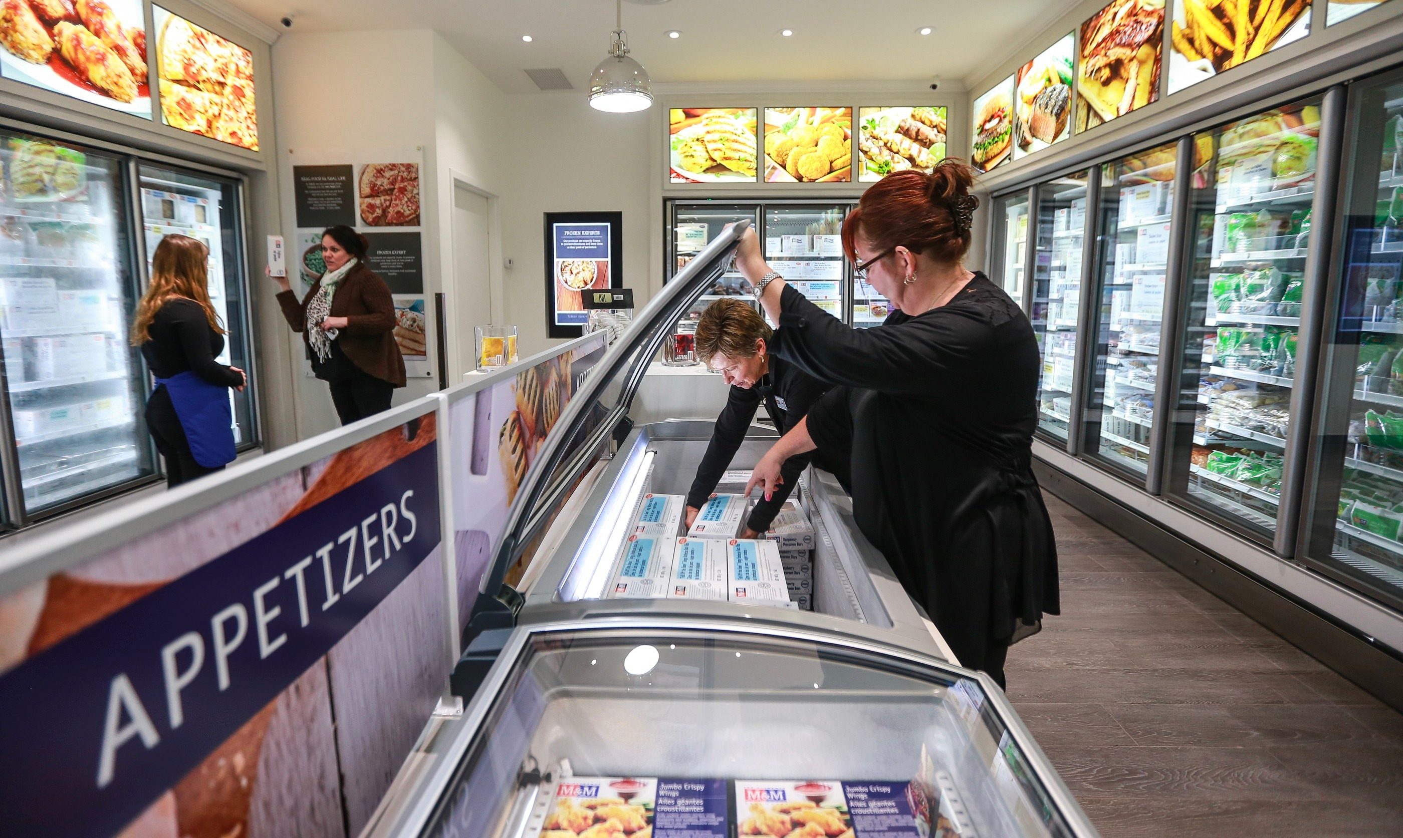 Two women standing in front of an opened M&M Food Market freezer.