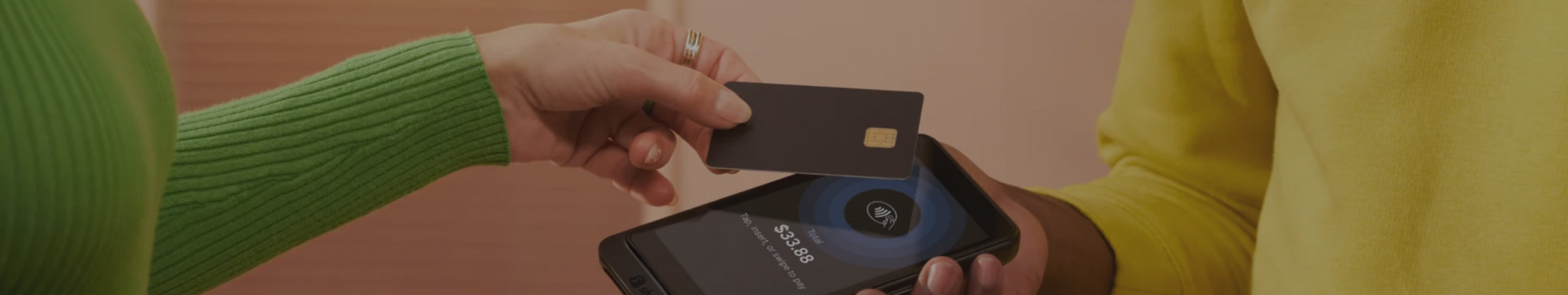 Close-up of a customer's hand holding a black credit card near a Shopify card reader to process a payment, capturing a moment of transaction.