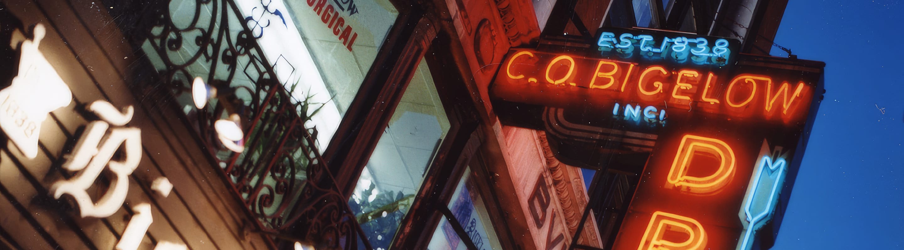 Neon sign for C.O. Bigelow on their store facade with a blue sky background.